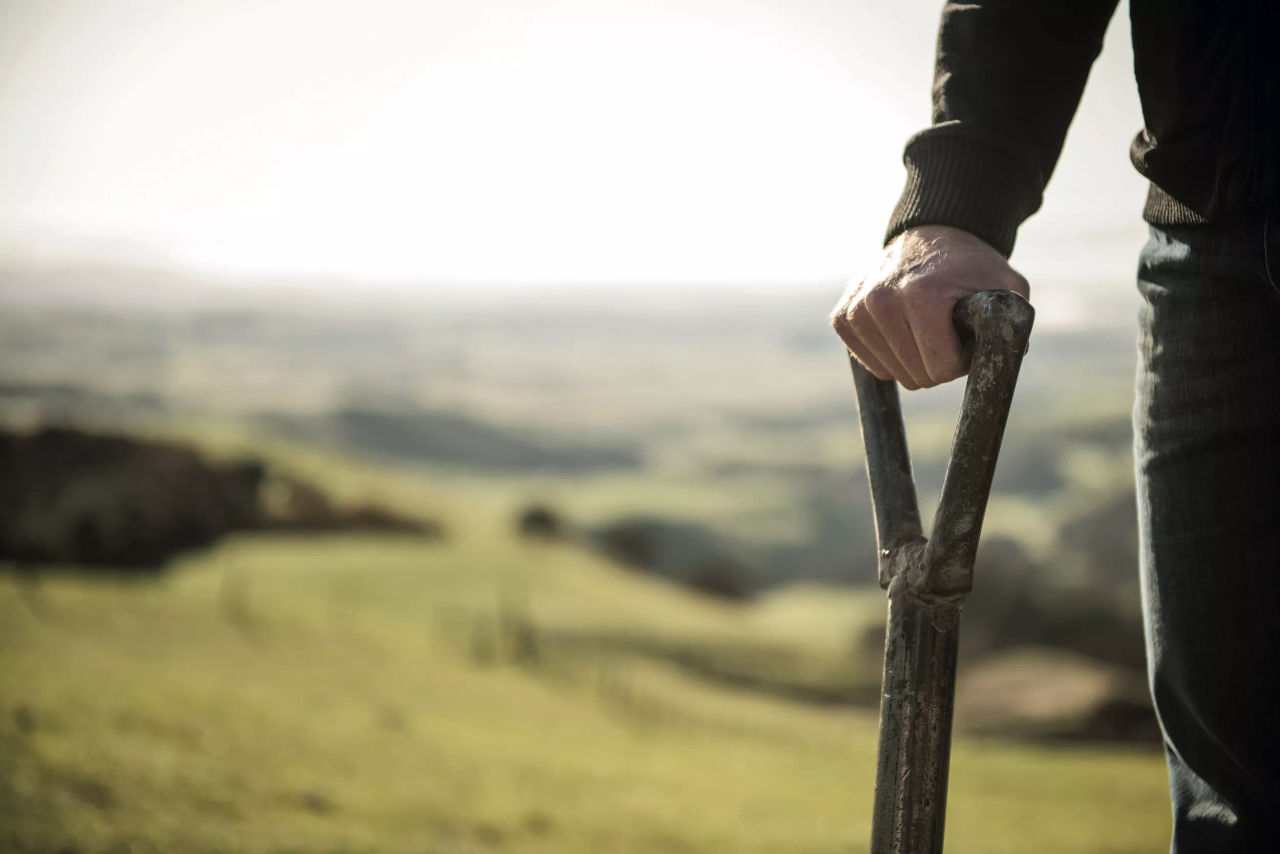The lower half of a farmer standing with a spade with rolling hills in the background